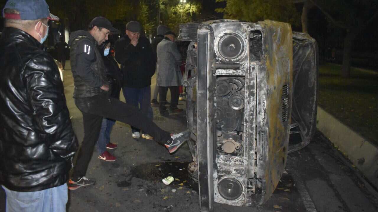 Protesters are seen near a burnt vehicle as they gather at the Presidential Palace to protest the results of the parliamentary election in Bishkek, Kyrgyzstan.