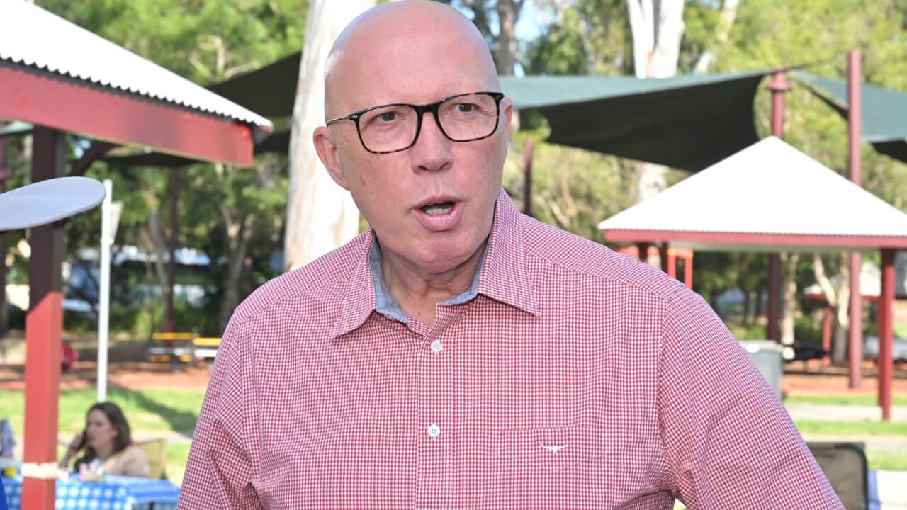 A man in a red shirt speaks as he stands in a park.