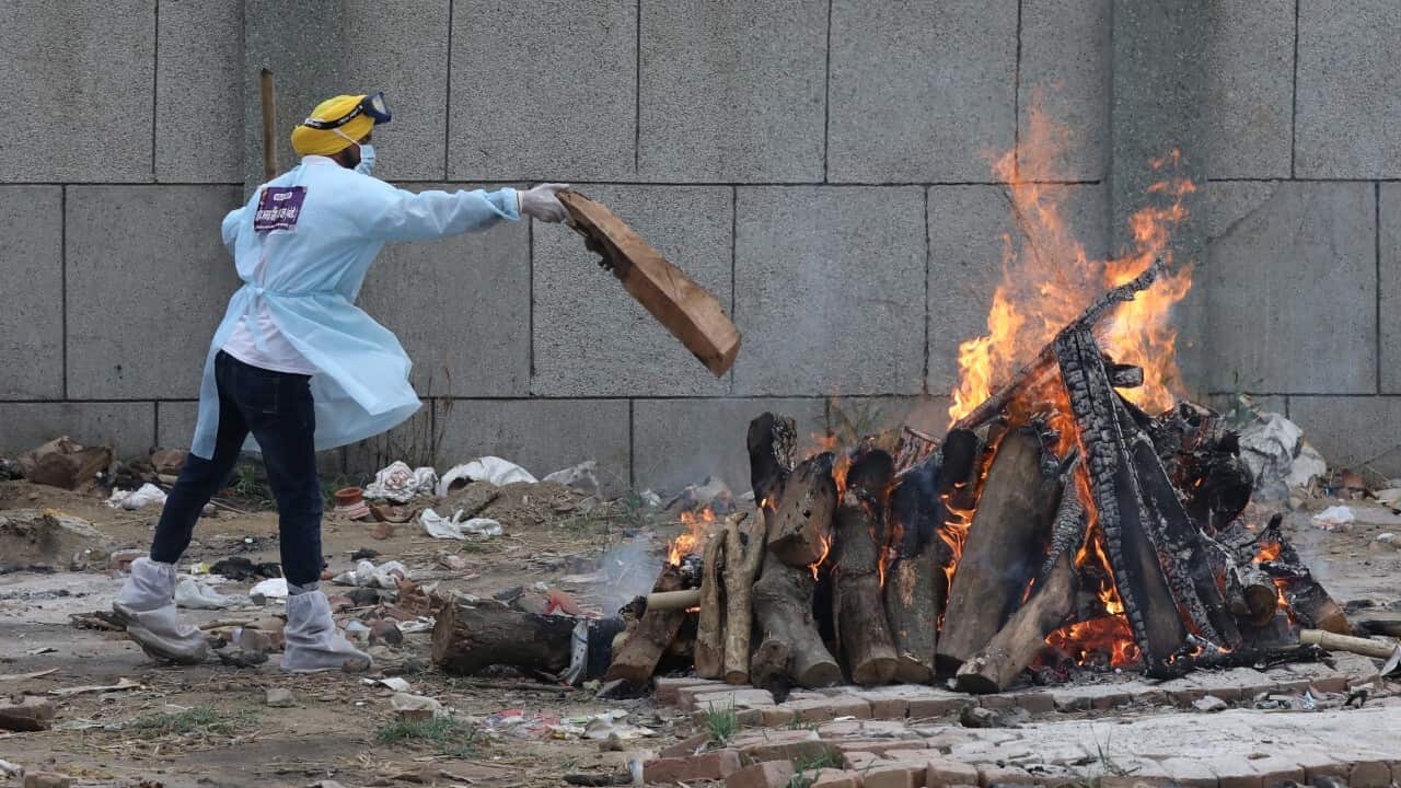 An Indian volunteers is seen near burning pyre during a mass funeral of Covid-19 victims at a ceremony in New Delhi, India, May18, 2021 (AAP)