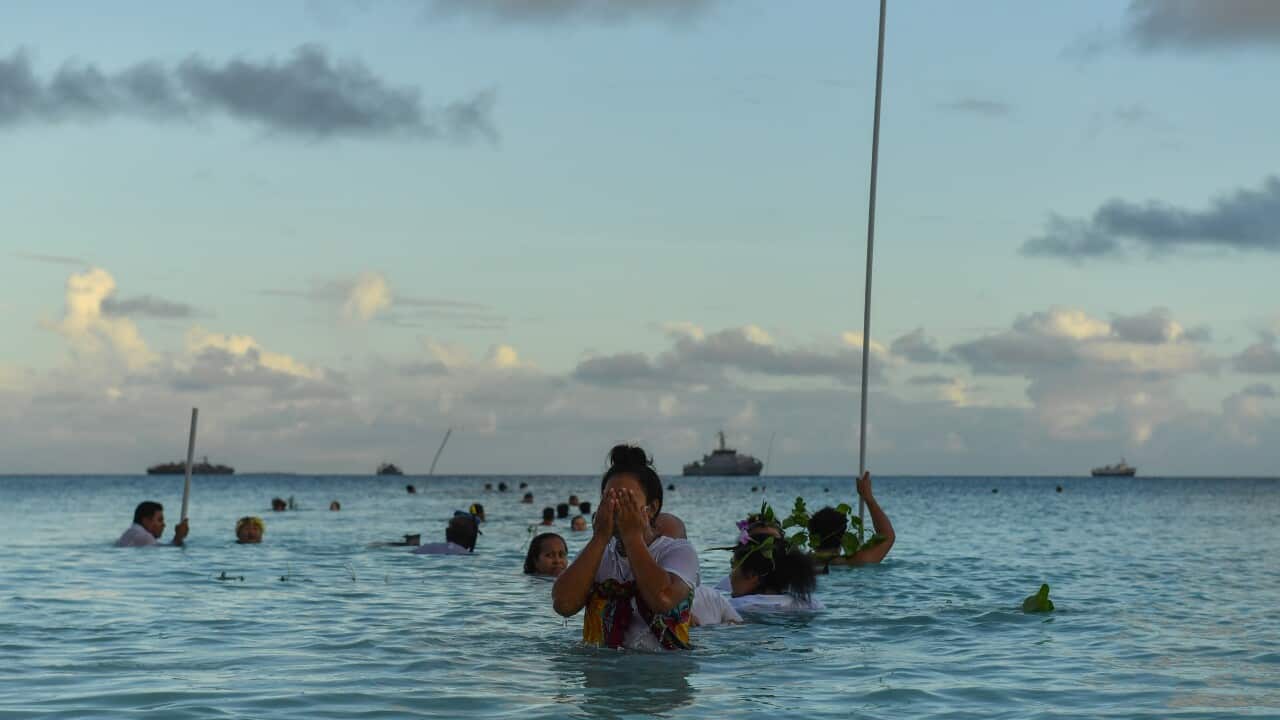 A woman covers her face while standing in the water with other people behind her