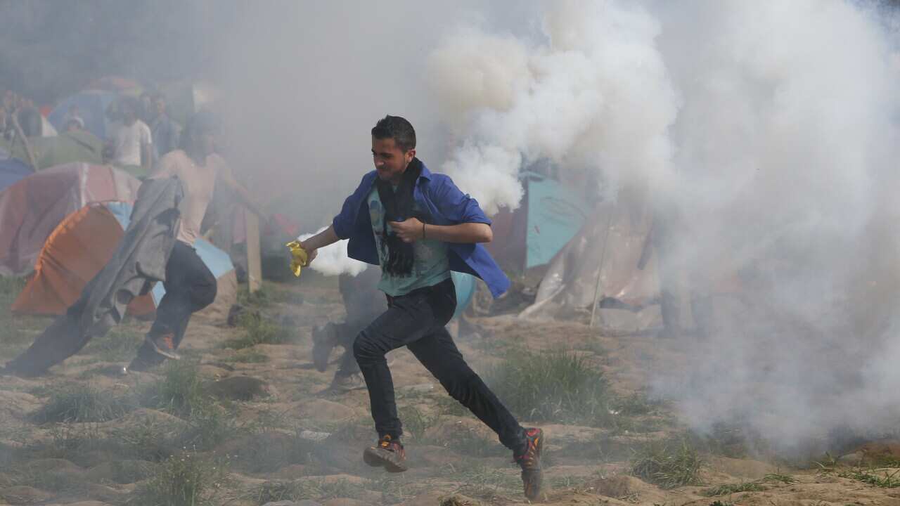 A man runs with a tear gas canister during clashes with Macedonian police at Idomeni, Greece
