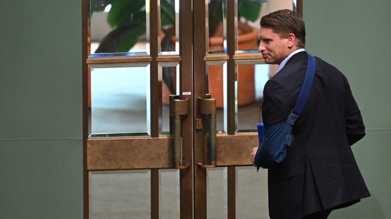 A man in a suit with his left arm in a blue sling walks toward a set of large, ornate double doors.
