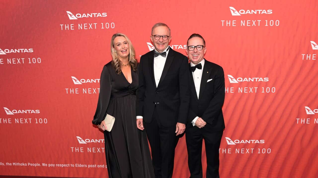 Anthony Albanese (centre) stands flanked by a woman and a man against a red background featuring Qantas logos.
