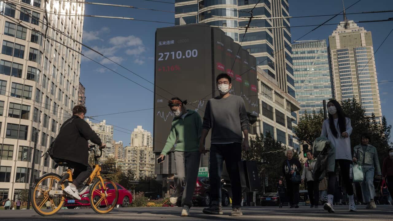 People walk on the street next to the large screen showing the newest stock exchange data in Shanghai