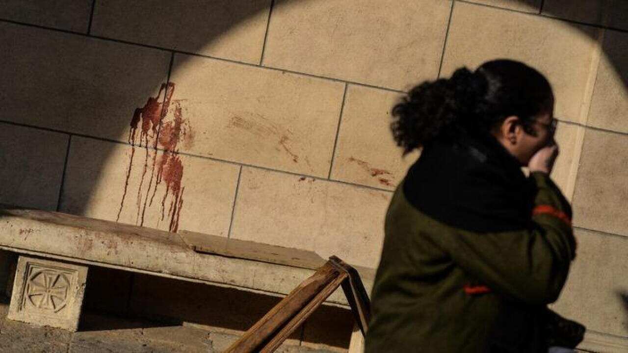 A woman walks past a blood-stained wall of the church (AAP)