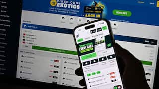 A smartphone with an app on its screen held in front of a laptop with a similar app on its screen.