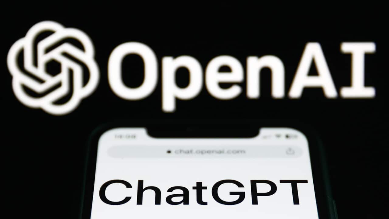 ChatGPT website displayed on a phone screen and OpenAI logo displayed on a screen in the background