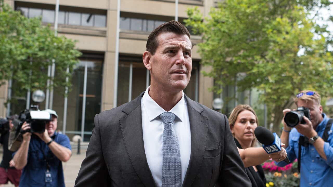 Ben Roberts-Smith wearing a black suit and blue tie walks with his chest puffed out