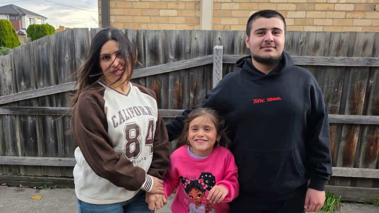 A woman, a young girl and boy standing together in front of a wooden fence.