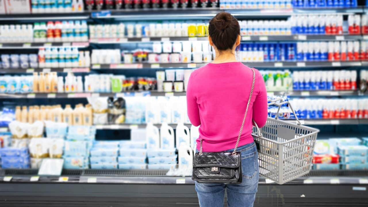 A woman looking in the dairy aisle at a supermarket.