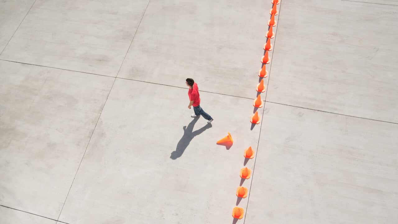Man walking away from row of traffic cones with one misplaced