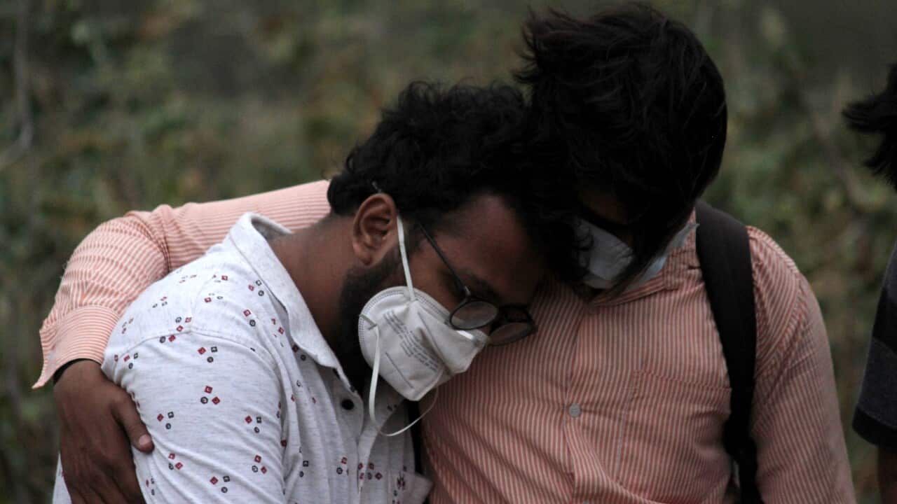A man is consoled by his relative during the burial of his father, who died of coronavirus, at a graveyard in New Delhi on 16 April, 2021.