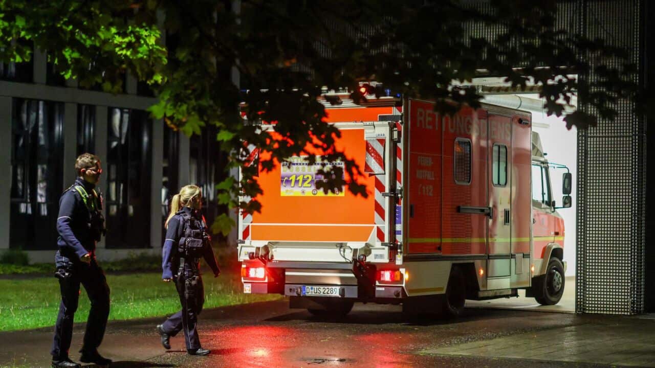 Police officers walk past an arriving ambulance taking a German patient to the infection center at Düsseldorf University Hospital Wednesday May 6 2026 in Düsseldor.jpg