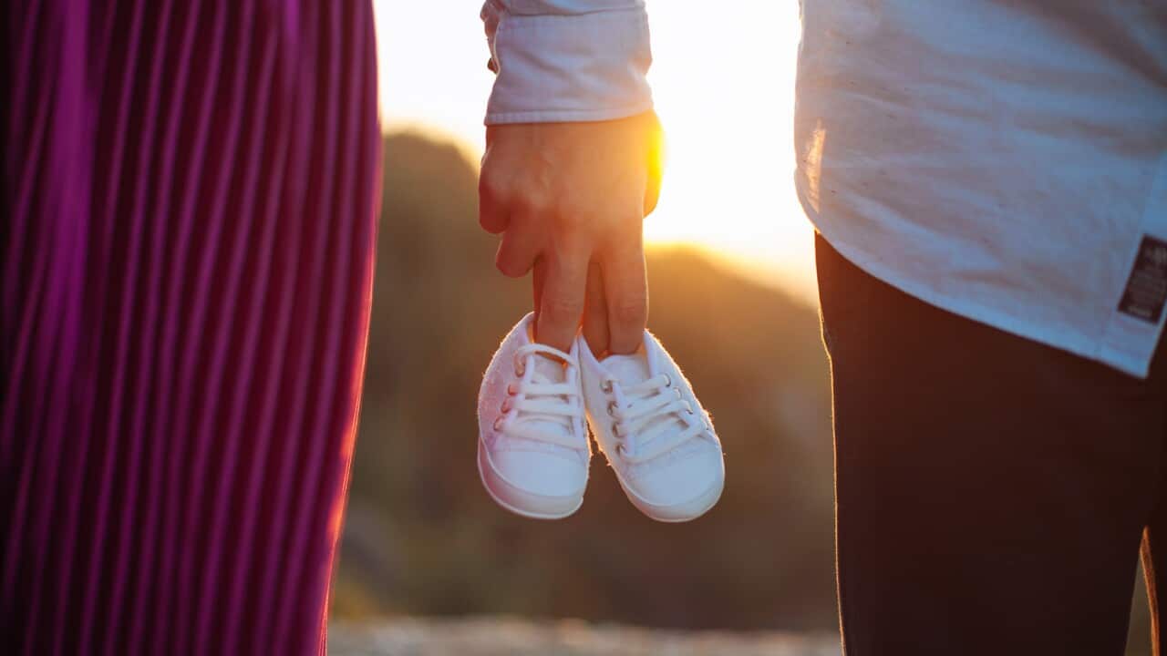 Parents holding hands and a pair of little baby shoes
