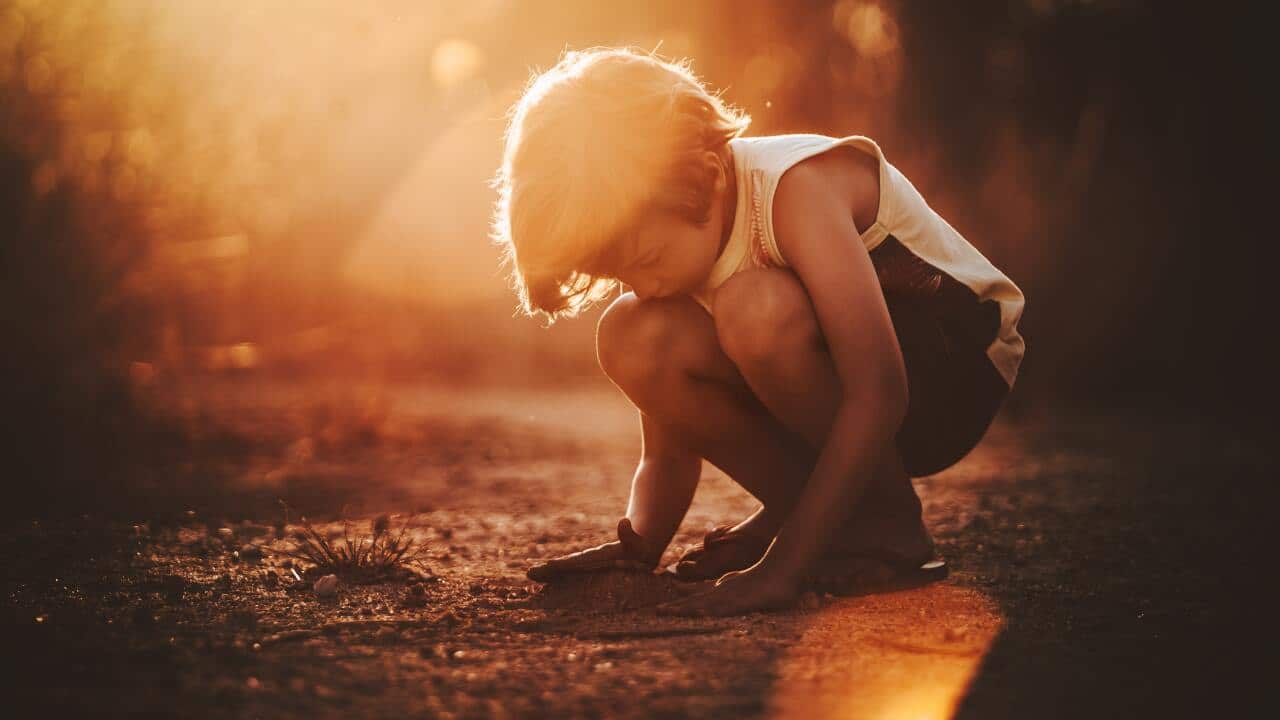 Little boy squatting on sandy ground.