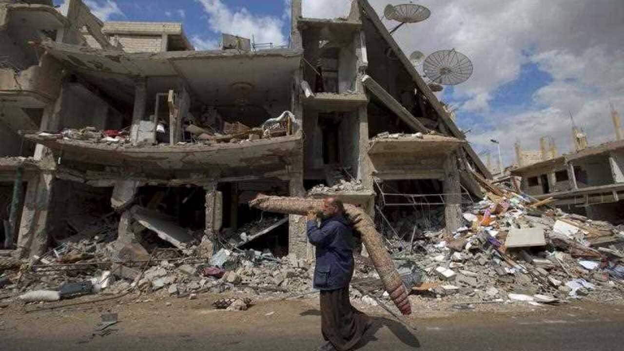 In this April 14, 2016 file photo, a Syrian man carries a carpet as he walks through a devastated part of the town of Palmyra