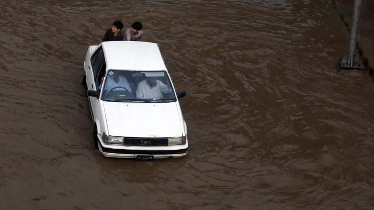 Pakistani boys push a car through a flooded street
