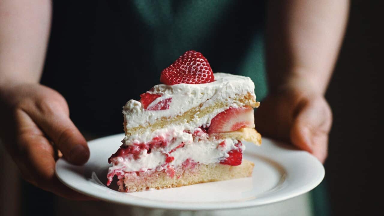 Woman in apron holding slice of strawberry cake
