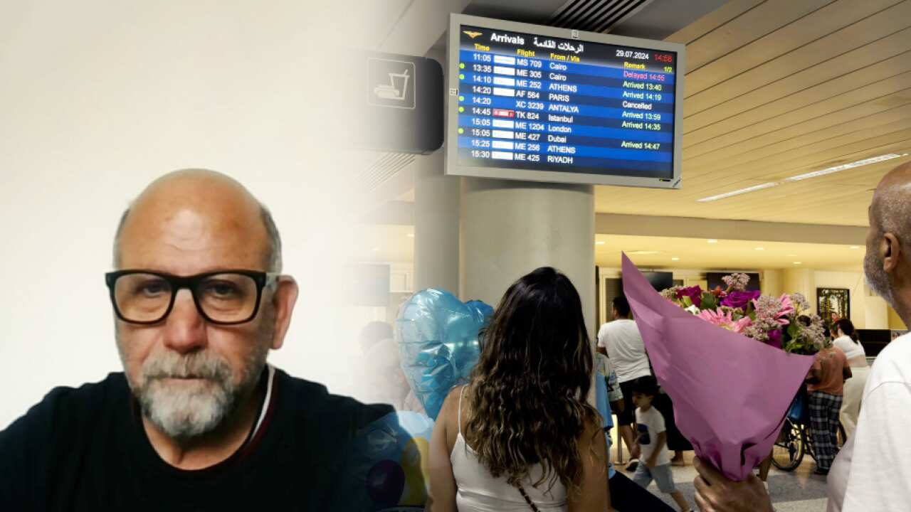 A man at the left and people staring at an airport flights board