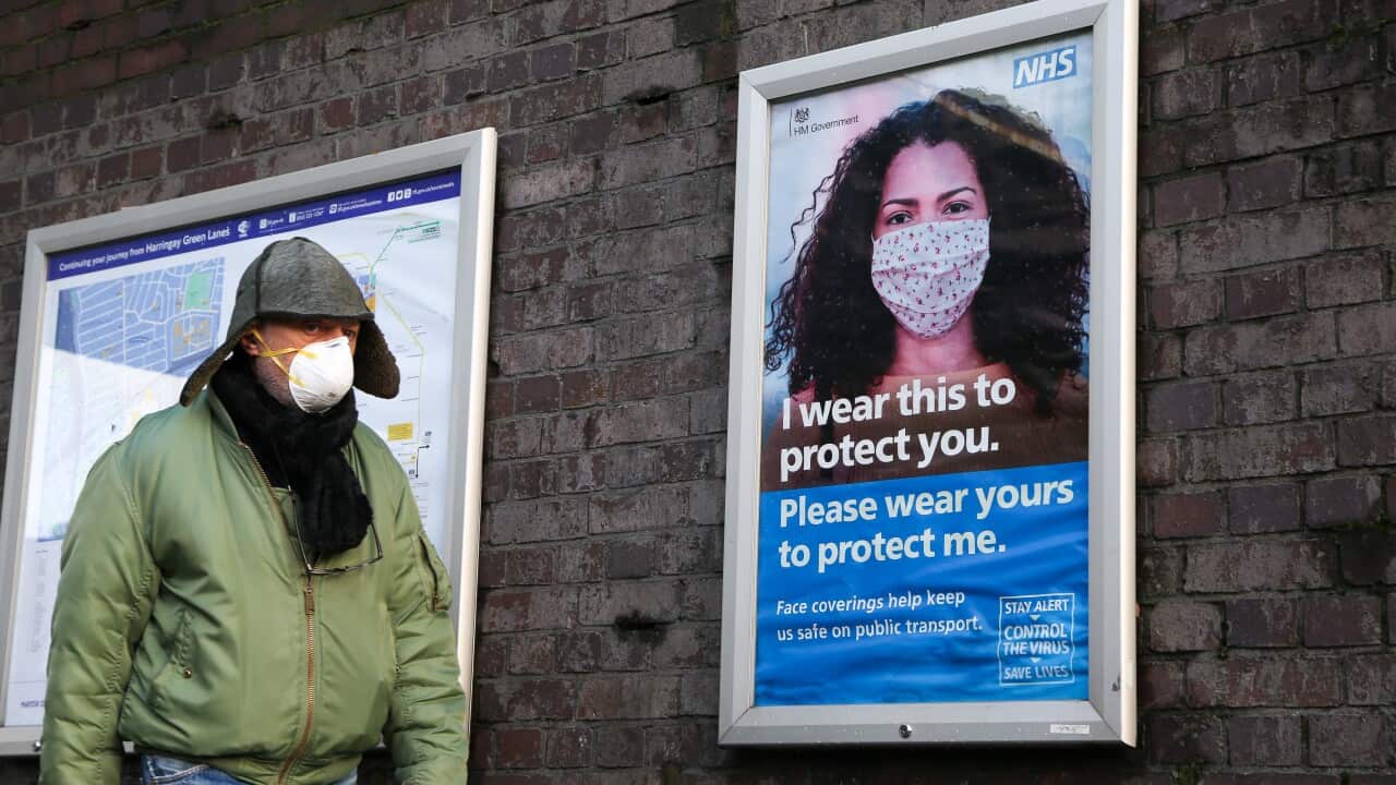A man wearing a face mask walk past the NHS COVID-19 public information campaign poster in London.
