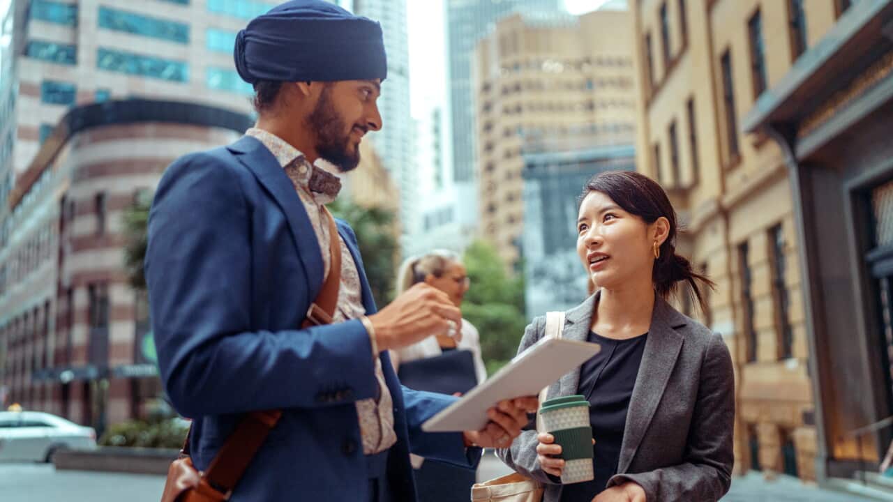 Two diverse colleagues discussing work while using digital tablet at city downtown