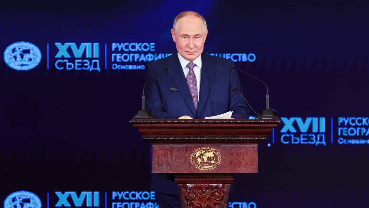 Vladimir Putin standing behind a podium on a stage speaking