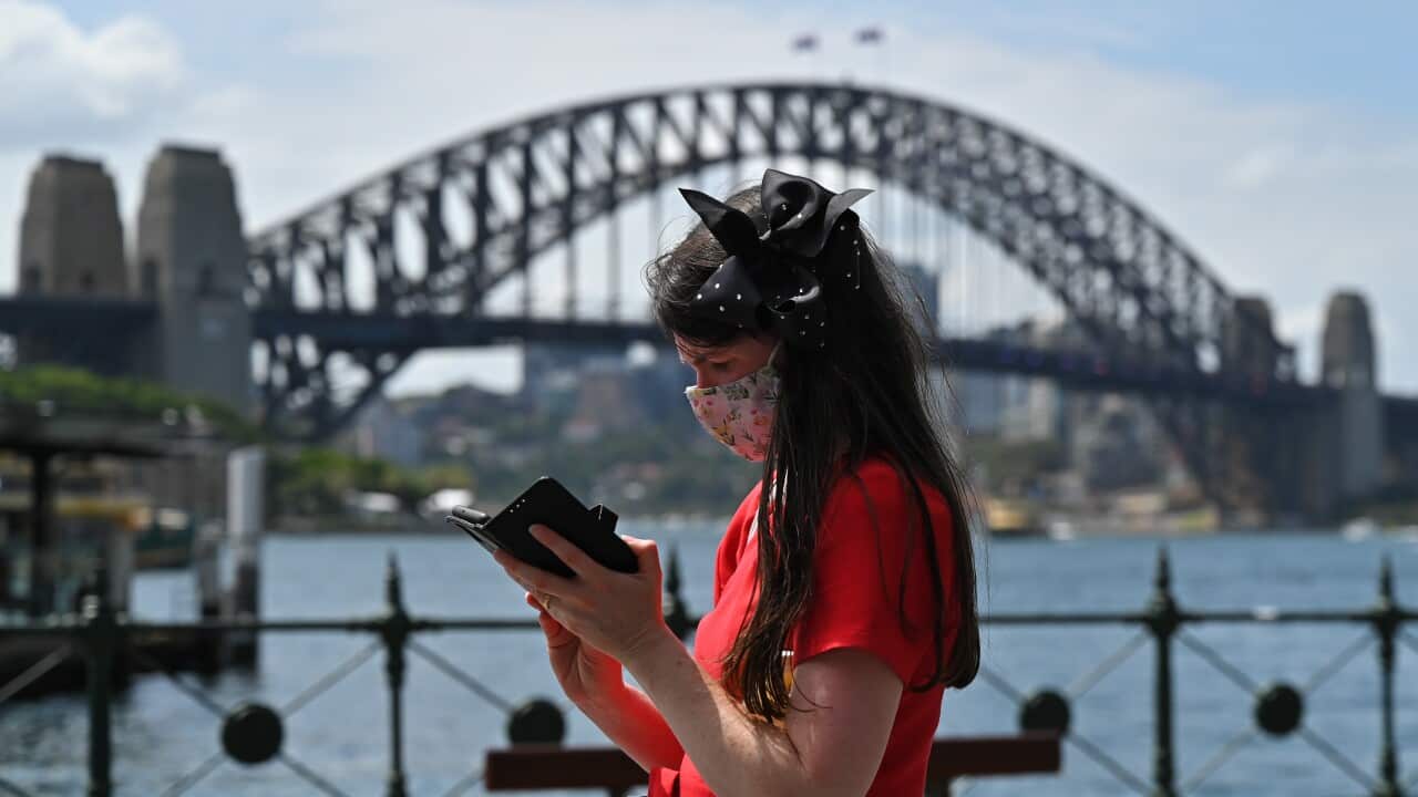 People wearing masks walk in front of the Sydney Harbour Bridge at Circular Quay in Sydney, Tuesday, January 25, 2022. (AAP Image/Steven Saphore) NO ARCHIVING