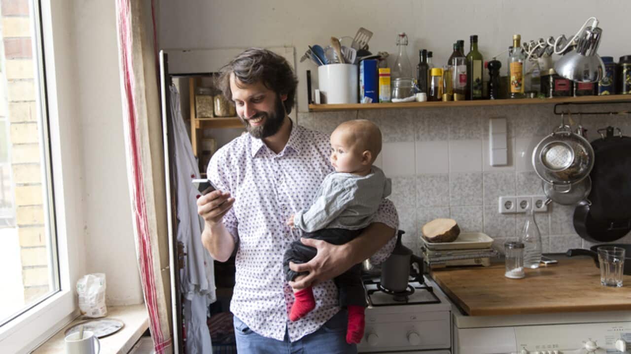 Father holding baby son while using smartphone.