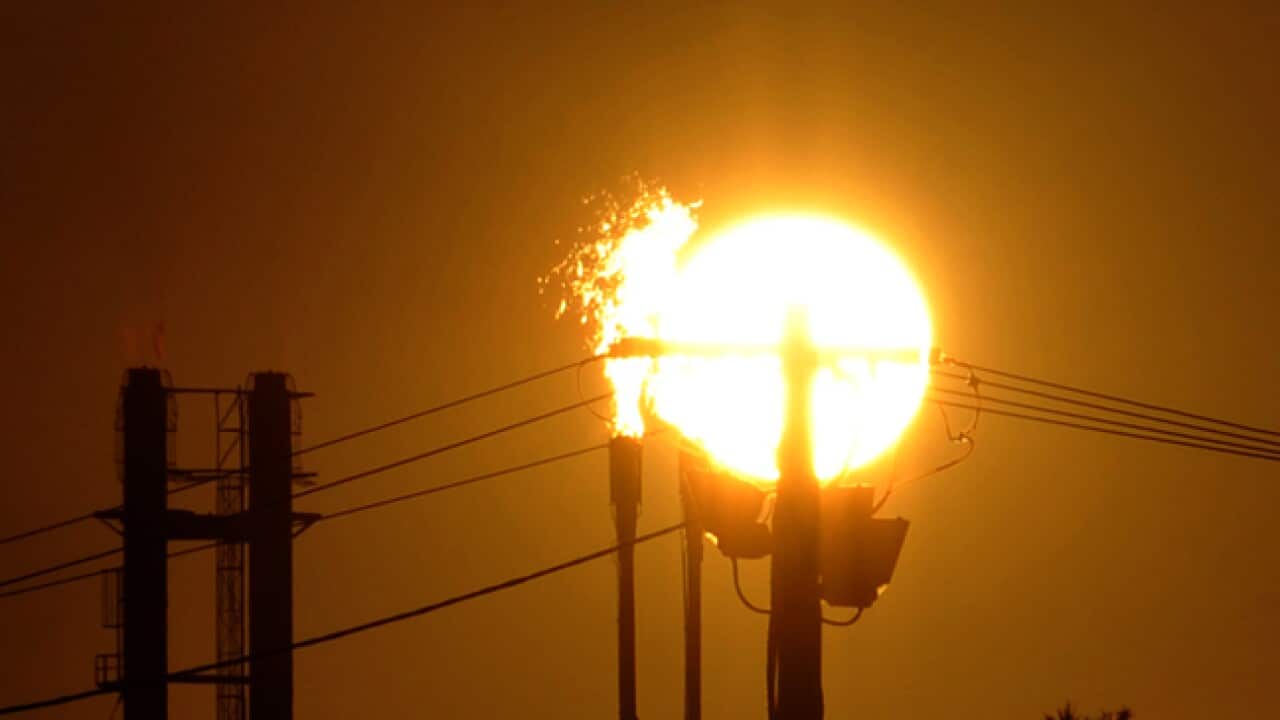 Industrial plant with flames coming out of a gas flare in front of a big, low yellow sun and amber sky