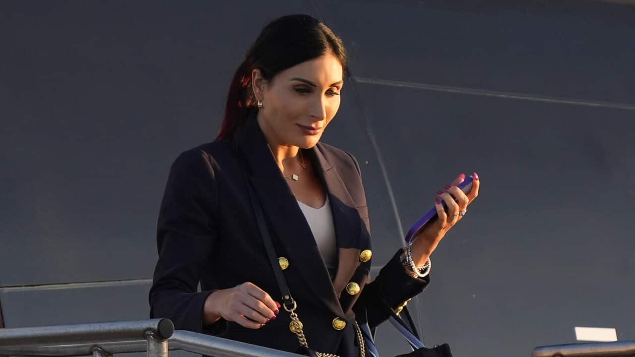 A woman wearing a black suit jacket and white top descending from a plane with a mobile phone in her hand.