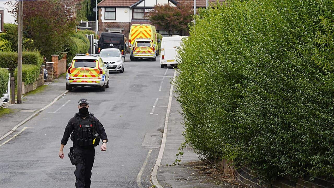 Police at the scene of an incident. There are emergency vehicles lined up in the area, cordoned off by police tape.