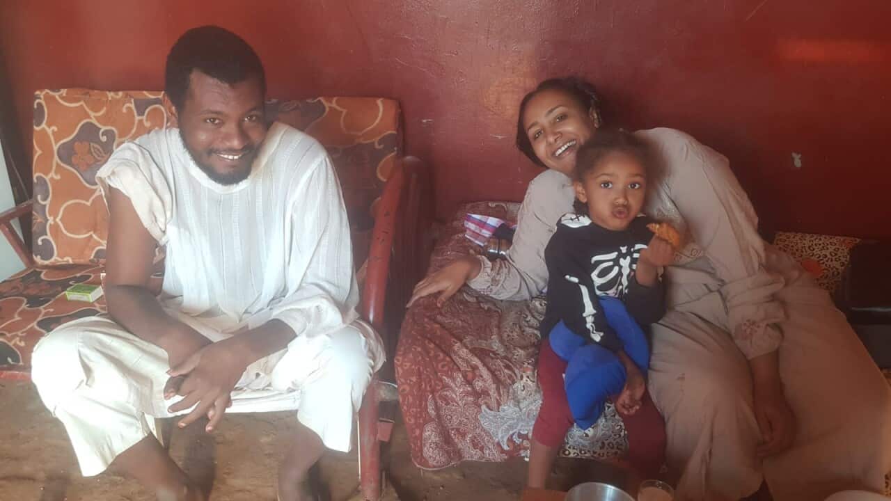 A man and a woman sitting and smiling for the camera. A small child is on the woman's lap.