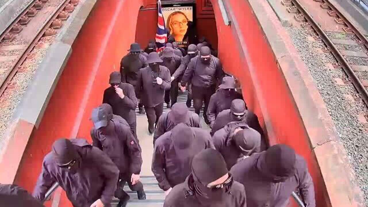 A group of about 40 men wearing black balaclavas and brandishing Australian flags at Artarmon train station in Sydney, Friday, January 26 (AAP).