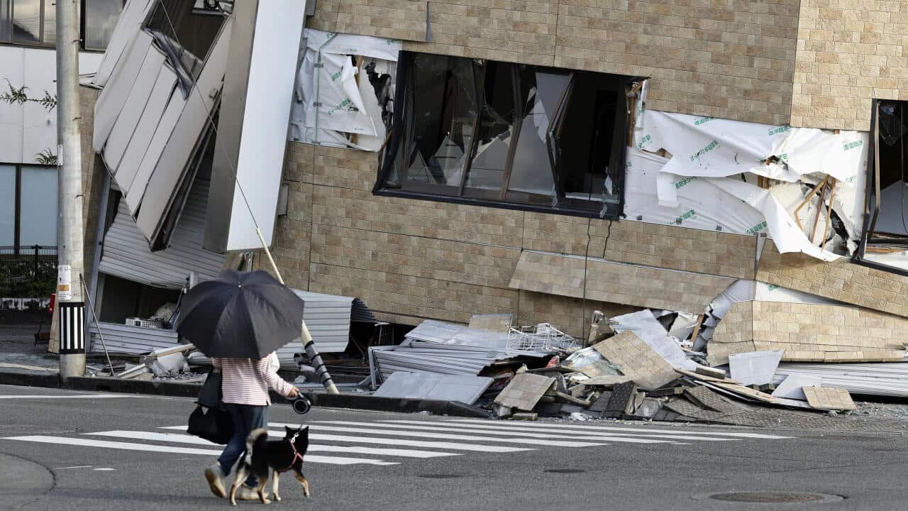 A person walks a dog on a leash past a collapsed brick building.
