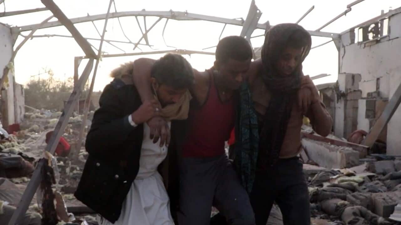 An injured man is being supported by two other men with rubble in the background.