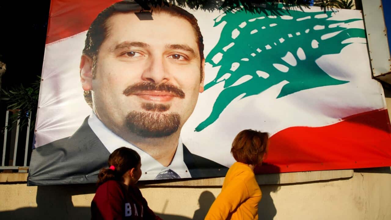 A woman and her daughter pass by a poster of outgoing Prime Minister Saad Hariri, in Beirut, Lebanon