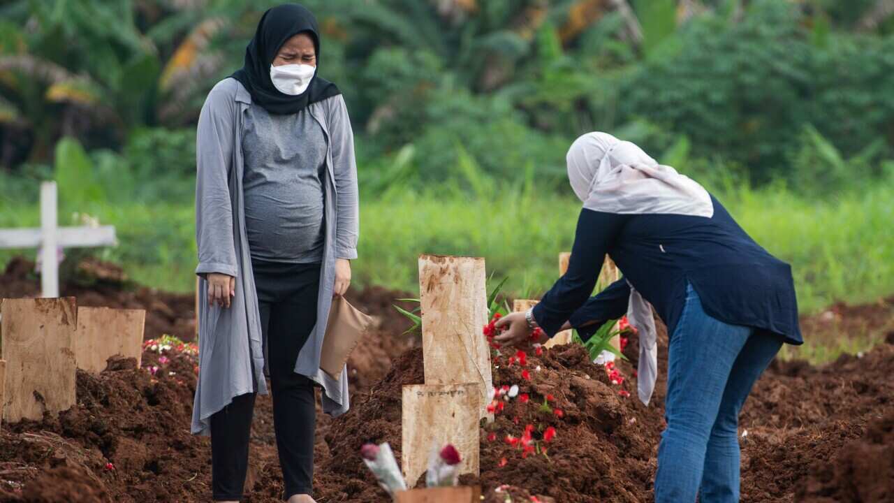 Relatives react after a COVID-19 victim is buried at a public cemetery in South Tangerang, Indonesia, on 27 June, 2021.