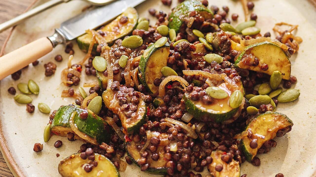 Tossed lentils and zucchin slices sit on a cream colouried plate.