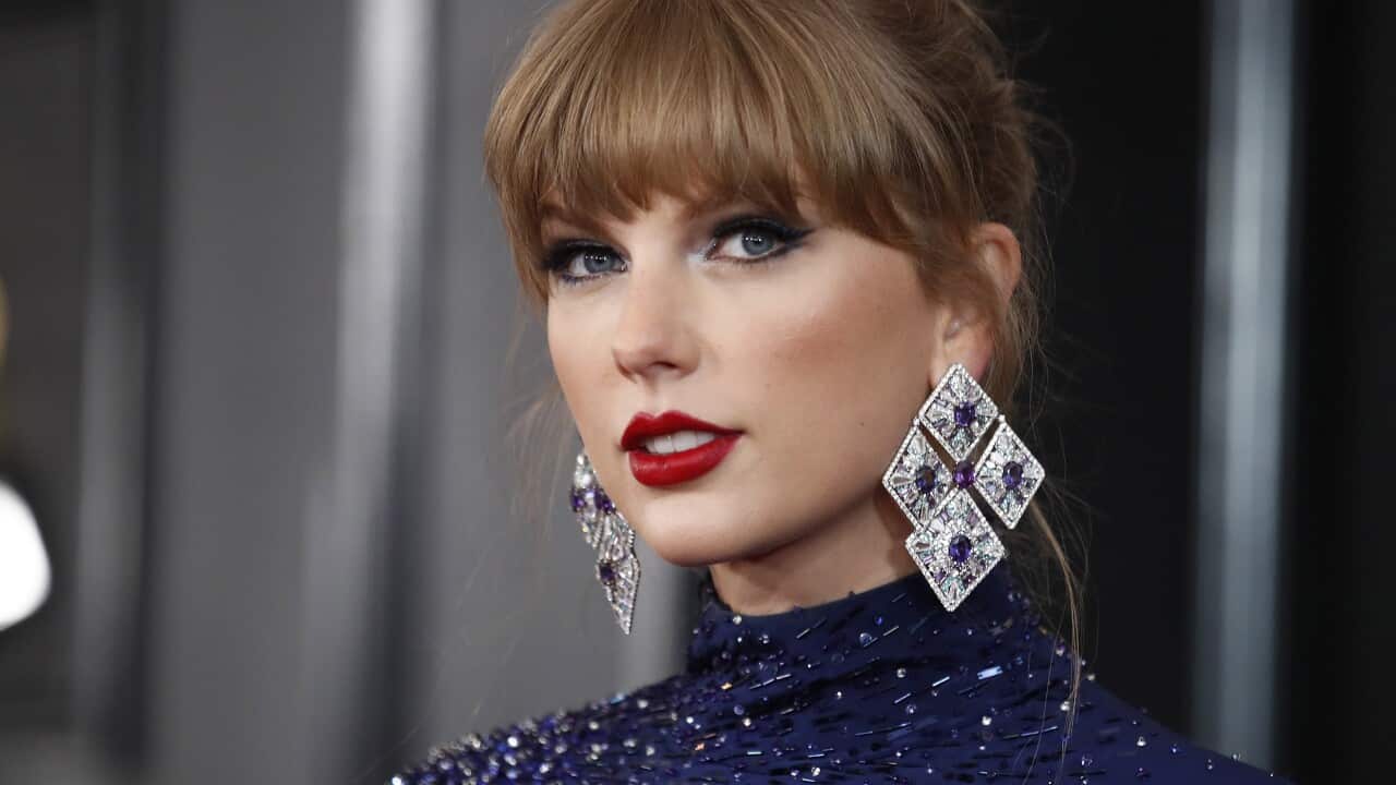 A photo of Taylor Swift at the Grammy Awards, wearing a sparkly blue dress and big sparkly earings, with her hair tied back.