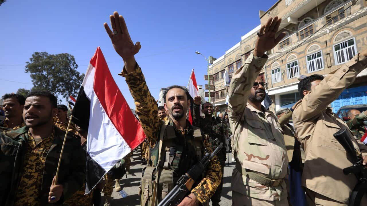 Armed militants raise their right arms in a salute alongside Yemeni flags