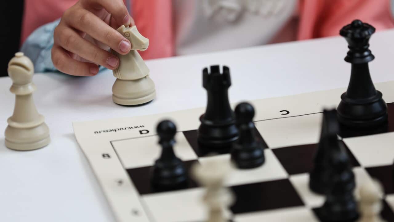 A chess board next to a person's hand holding the knight piece.