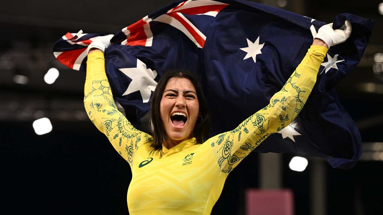 Saya Sakakibara, wearing a yellow long-sleeved top holds an Australian flag above her head in the air.