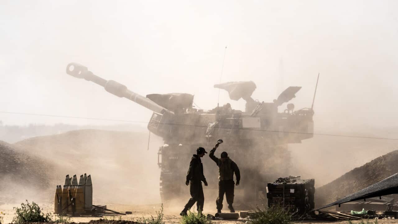 Two soldiers stand silhouetted in front of a tank, the barrel of which juts to one side. The air behind the soldiers is dusty and the sky is a glaring white.
