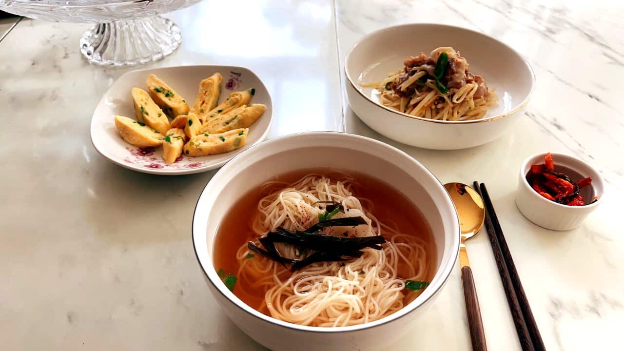 Hot oil noodle soup, egg and dumplings in bowls with chopsticks and a spoon on a marble table.