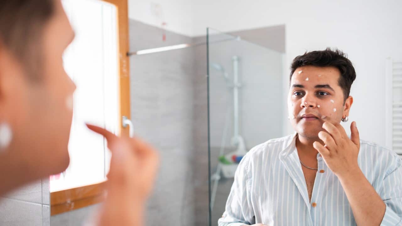 Man applying face cream while looking in the bathroom mirror