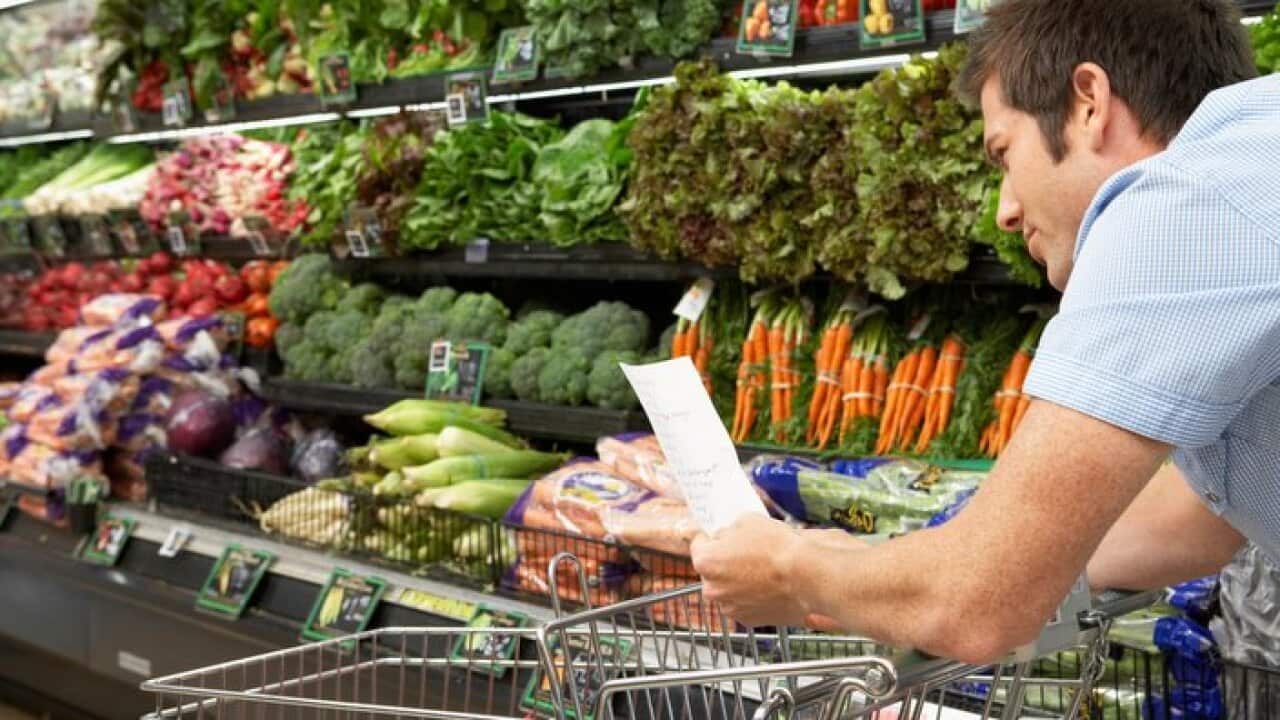 Young man reading shopping list in produce aisle, side view, close-up