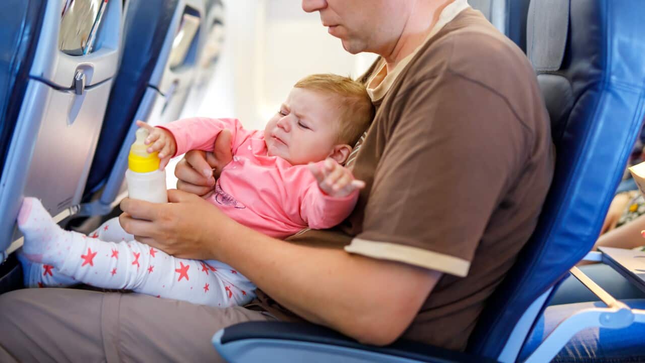 Young tired father and his crying baby daughter during flight on airplane going on vacations