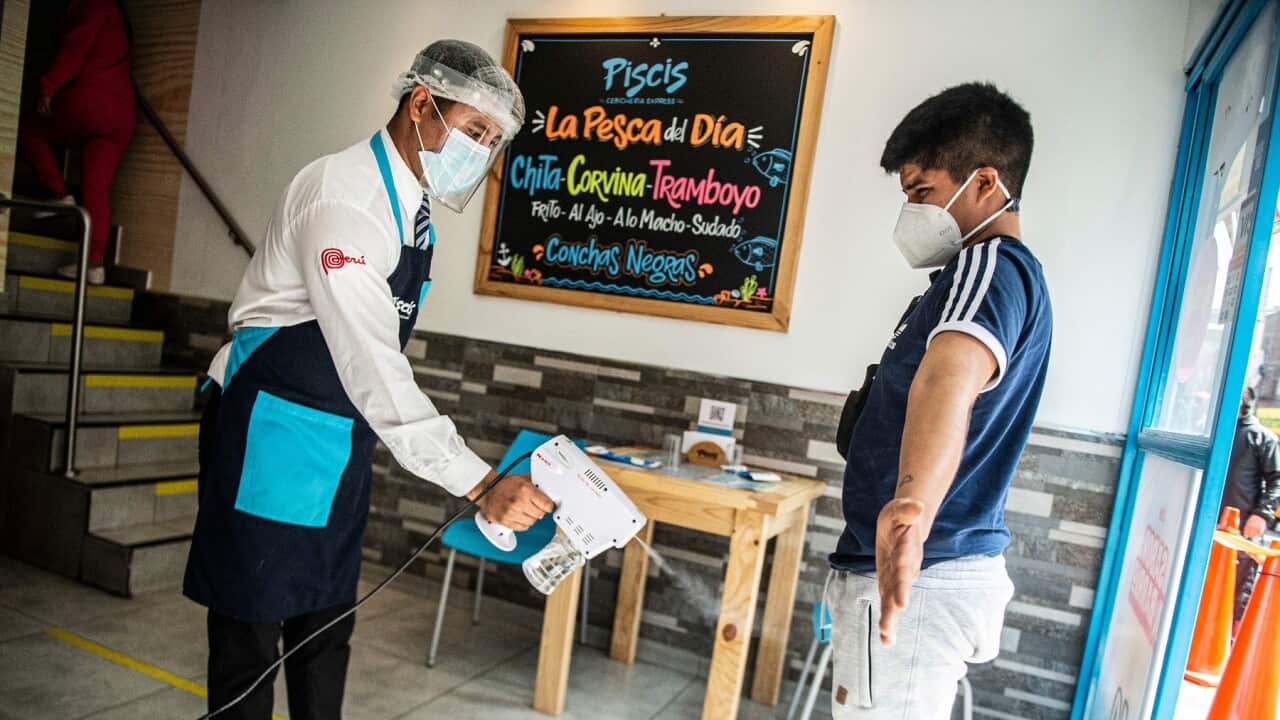 A waiter disinfects a customer as he enters a restaurant in Lima