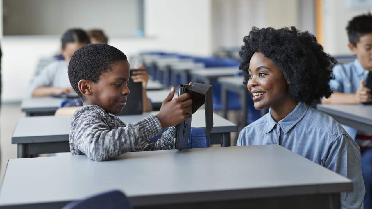 Teacher assisting boy working tablet at school