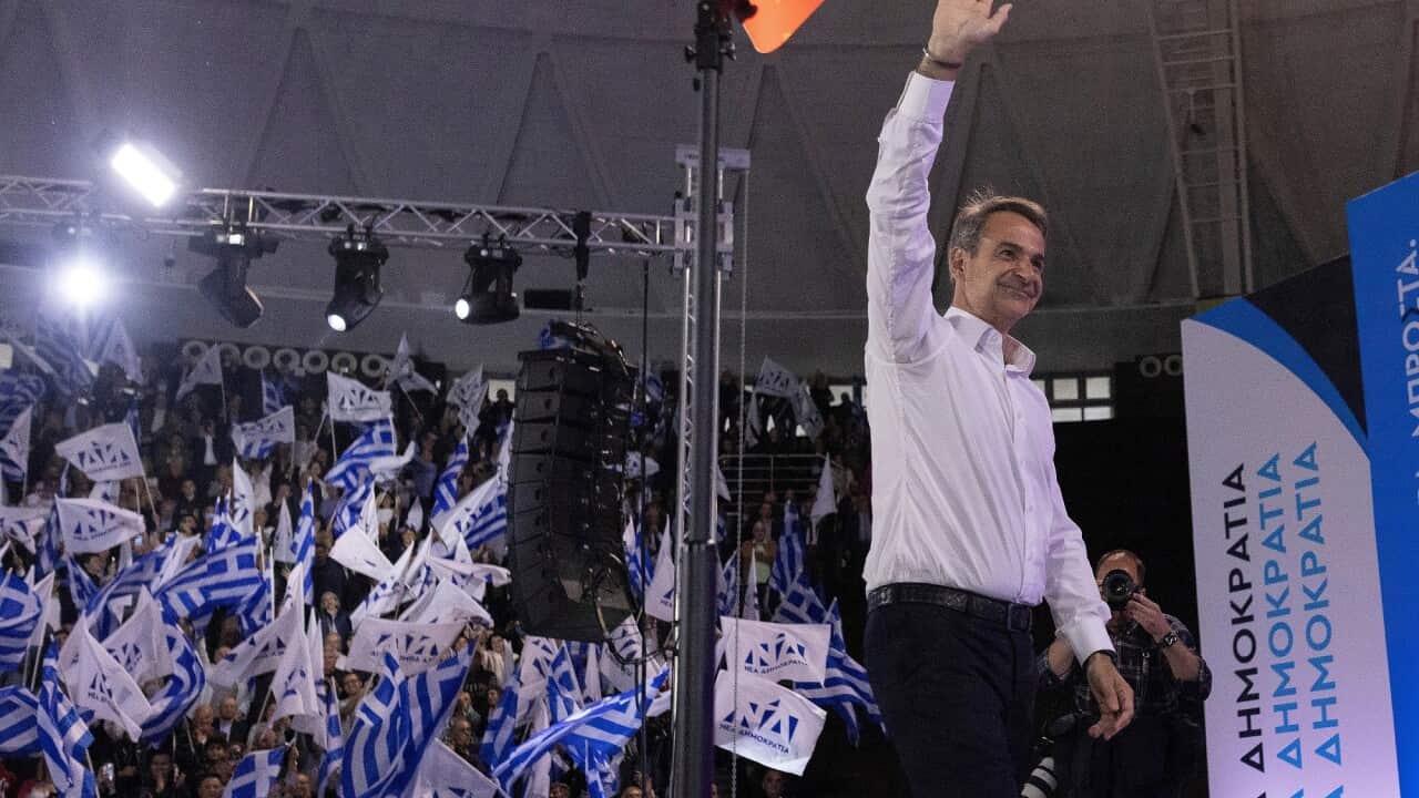Greek Prime Minister Kyriakos Mitsotakis waves to party supporters who are holding flags at an election rally.